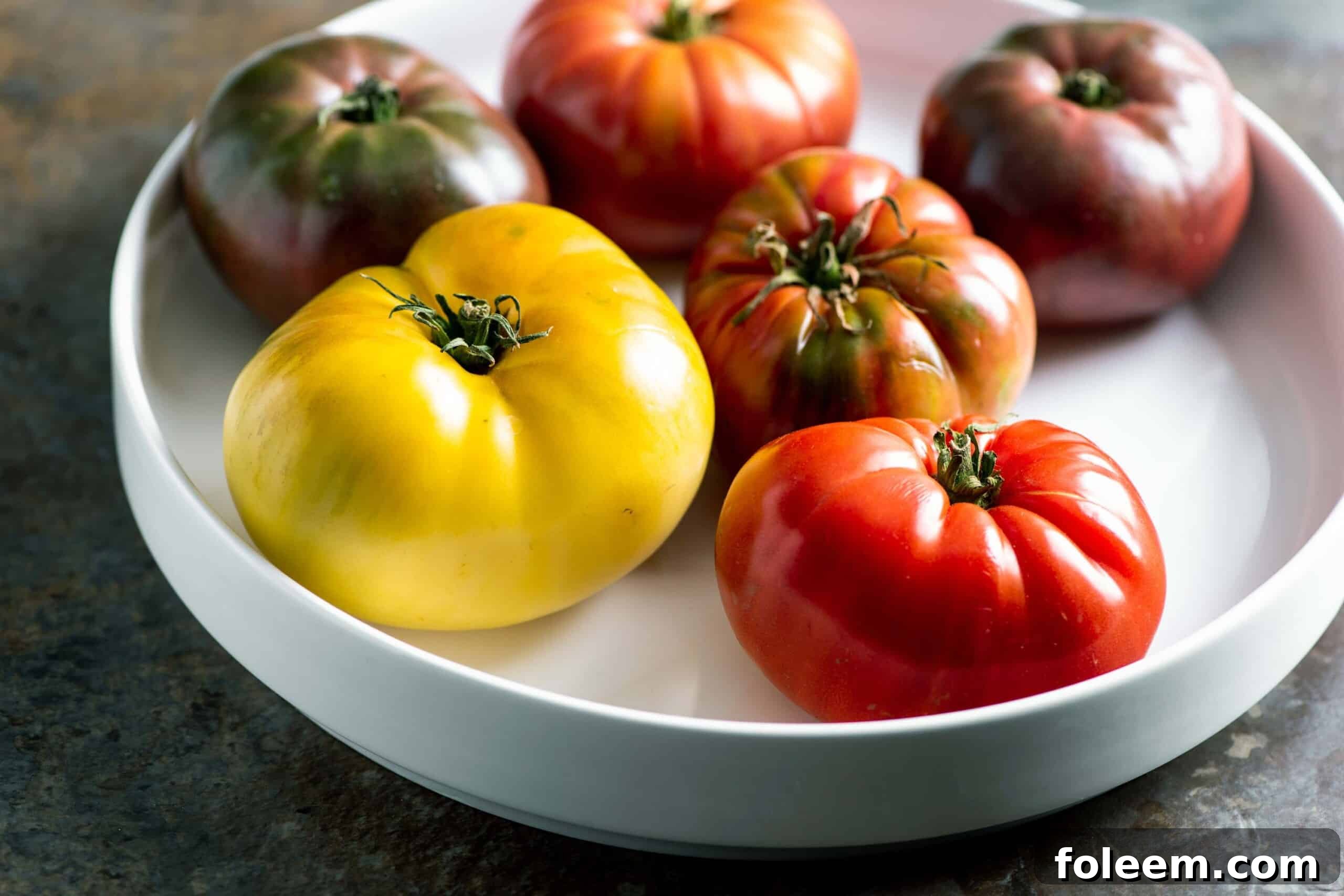 A variety of heirloom tomatoes ripening on white plate.
