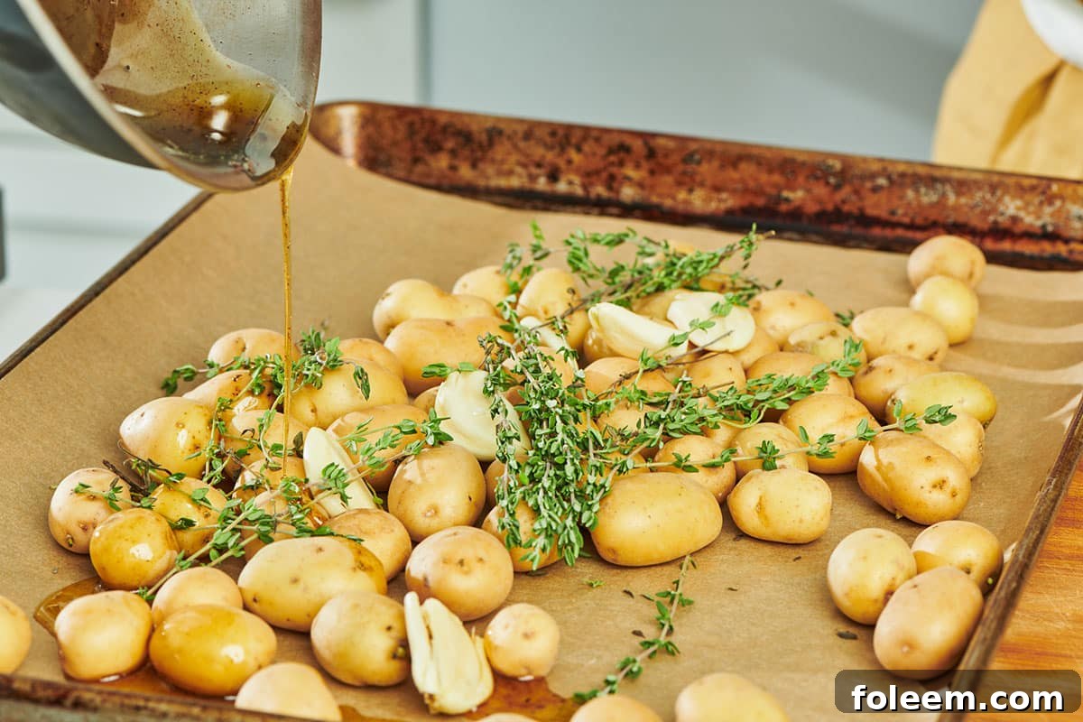 Drizzling duck fat over fresh thyme and potatoes on baking sheet.
