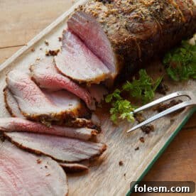 Sliced eye of round roast with thyme and rosemary on cutting board.