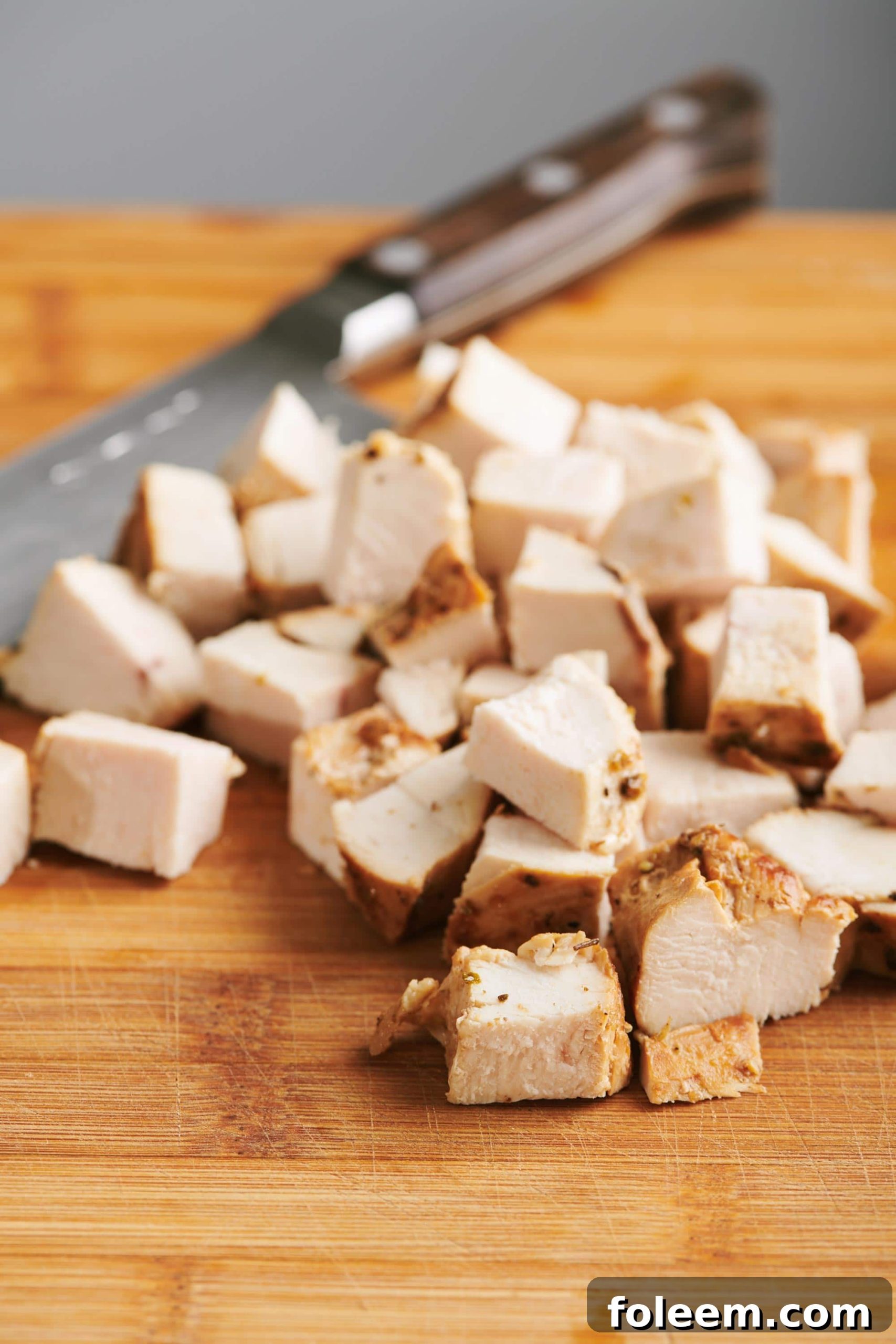 Cubed cooked chicken breast on a cutting board with a knife.