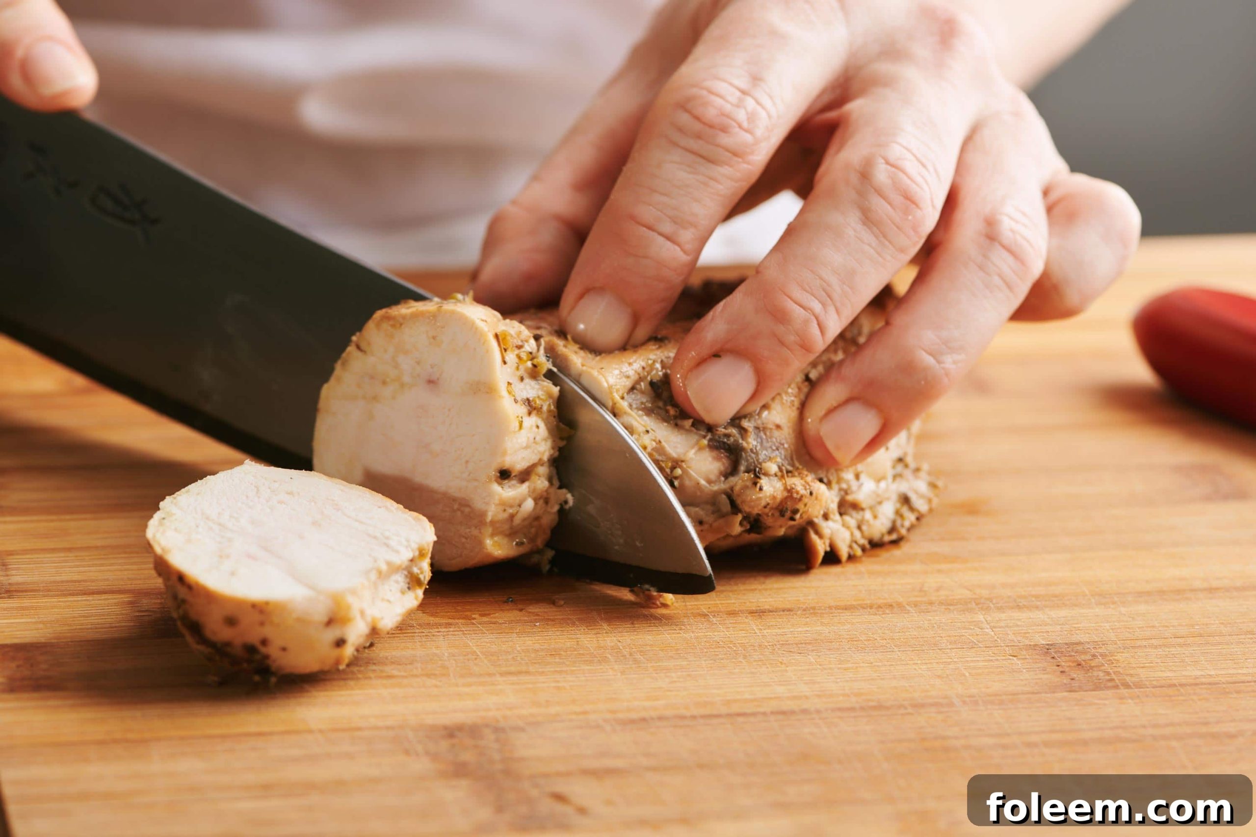 Woman slicing cooked chicken breast.