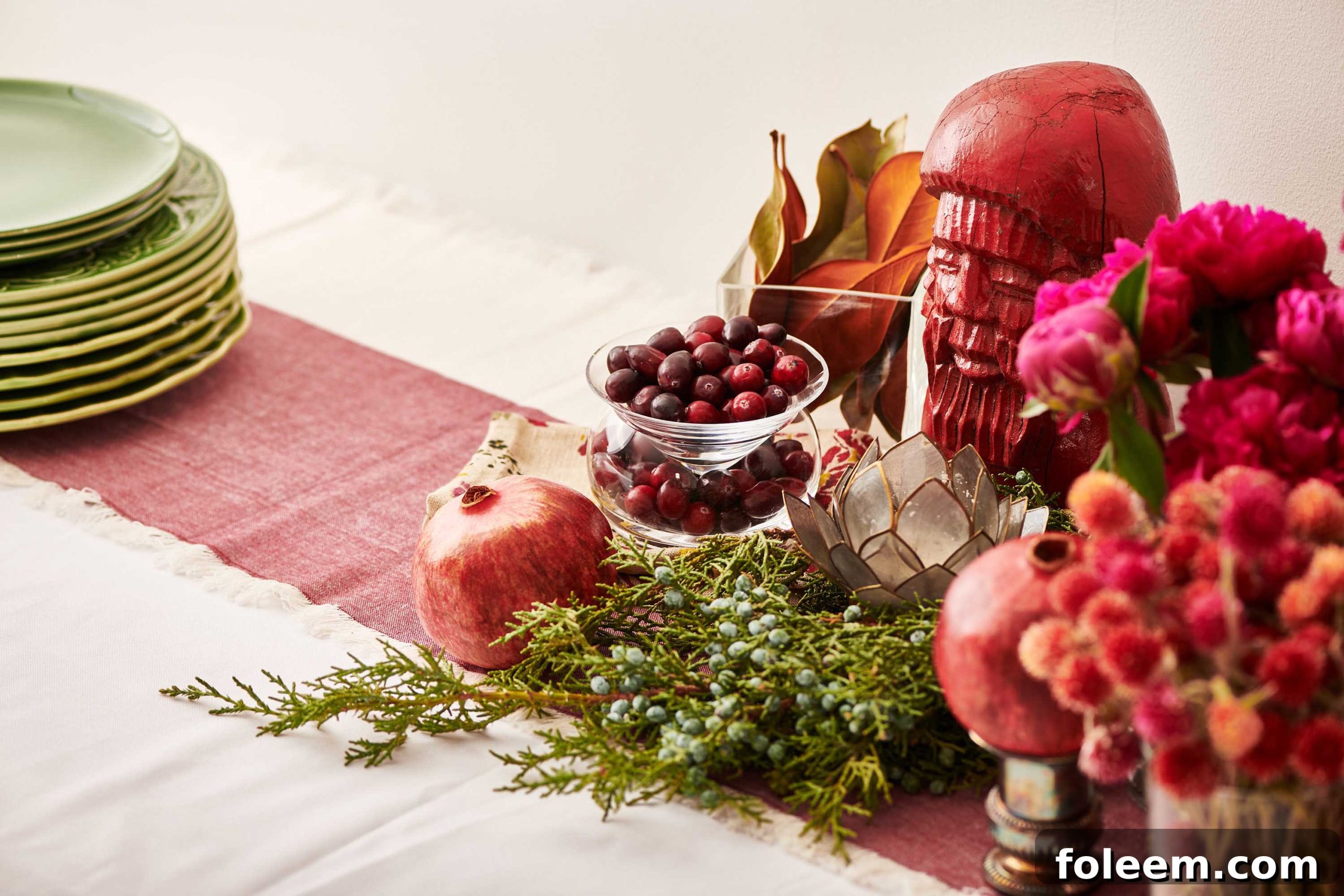 Red table runner topped with greenery, flowers, fruit, and decorations.