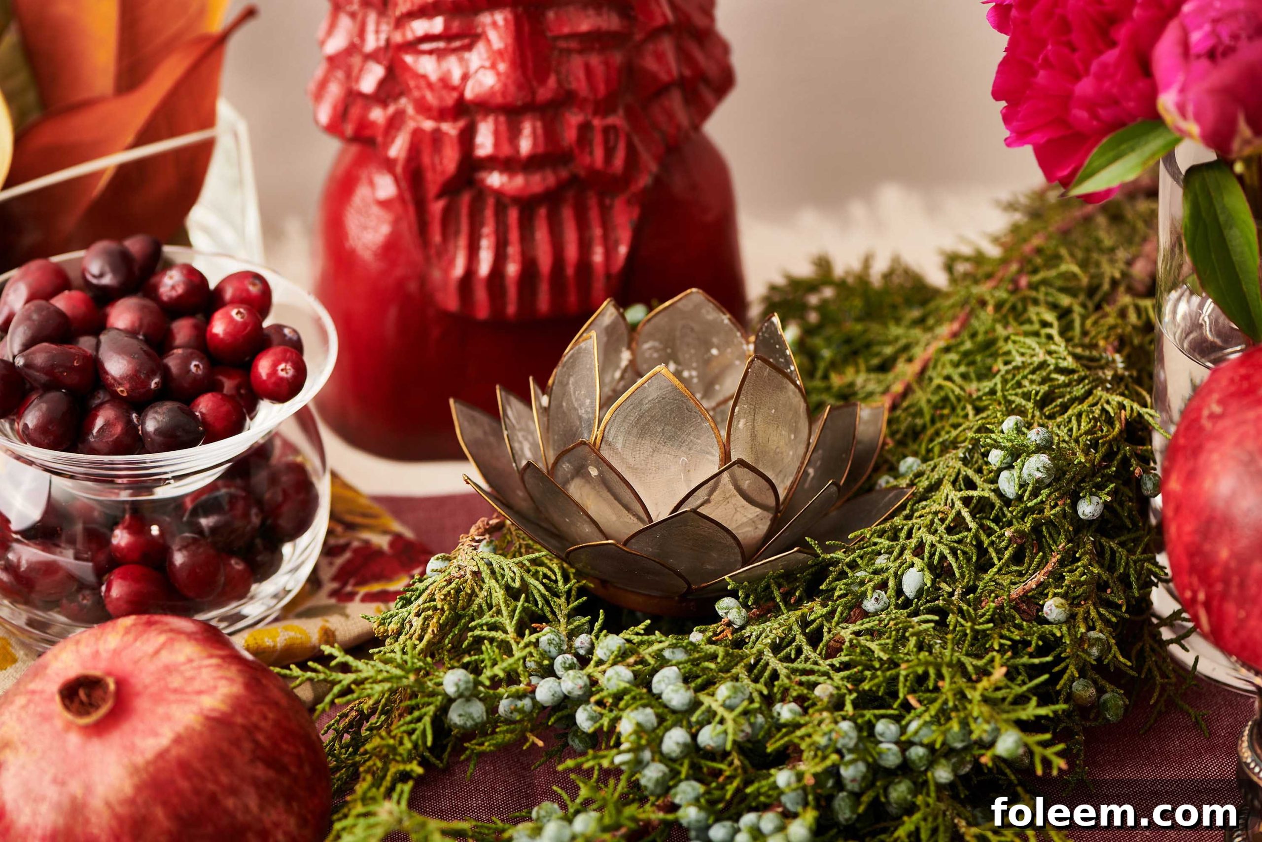 Red table runner topped with a carved red statue, greenery, and a candle holder.