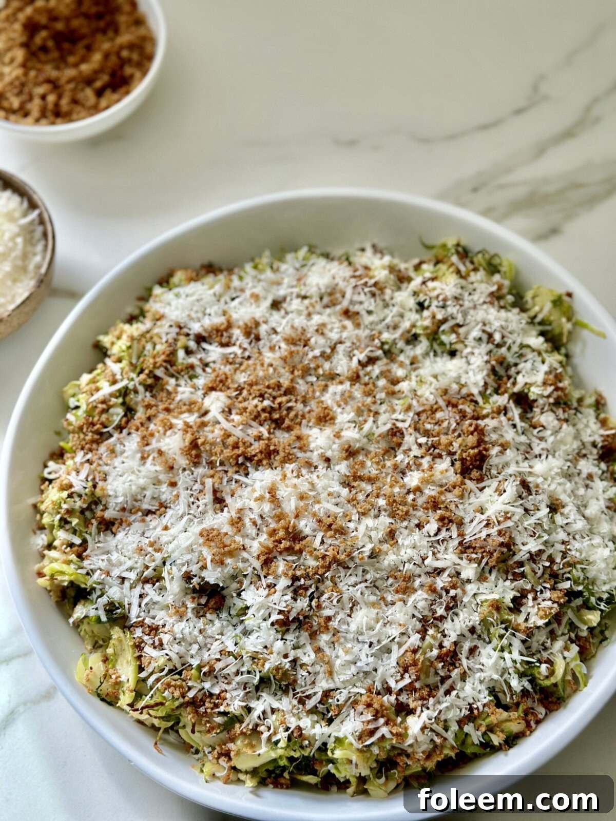 a brussels sprouts caesar salad in a white bowl topped with toasted breadcrumbs and parmesan cheese