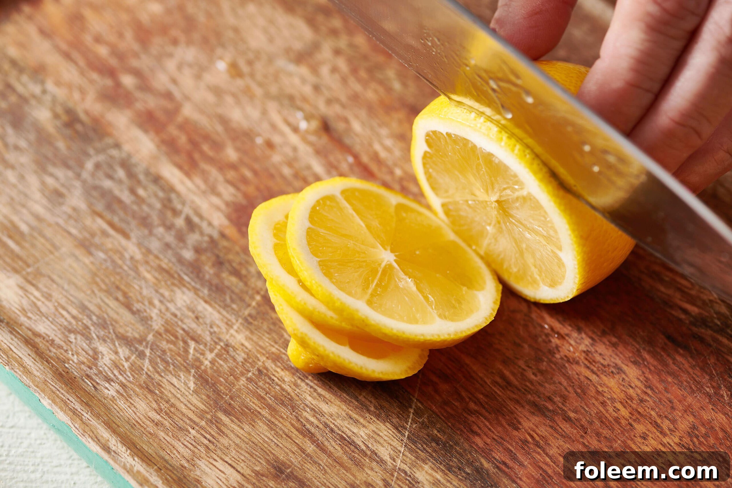 Partially sliced lemon on a wooden cutting board.