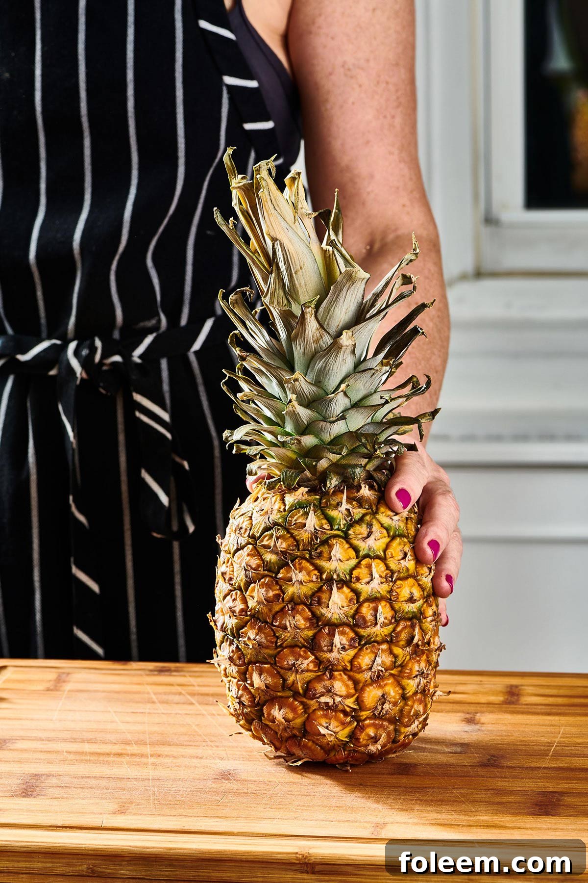 Woman holding fresh pineapple on cutting board.