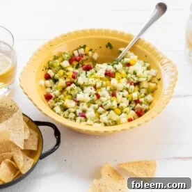 Yellow bowl with Pineapple Mint Jalapeno Salsa on table with chips and drinks.