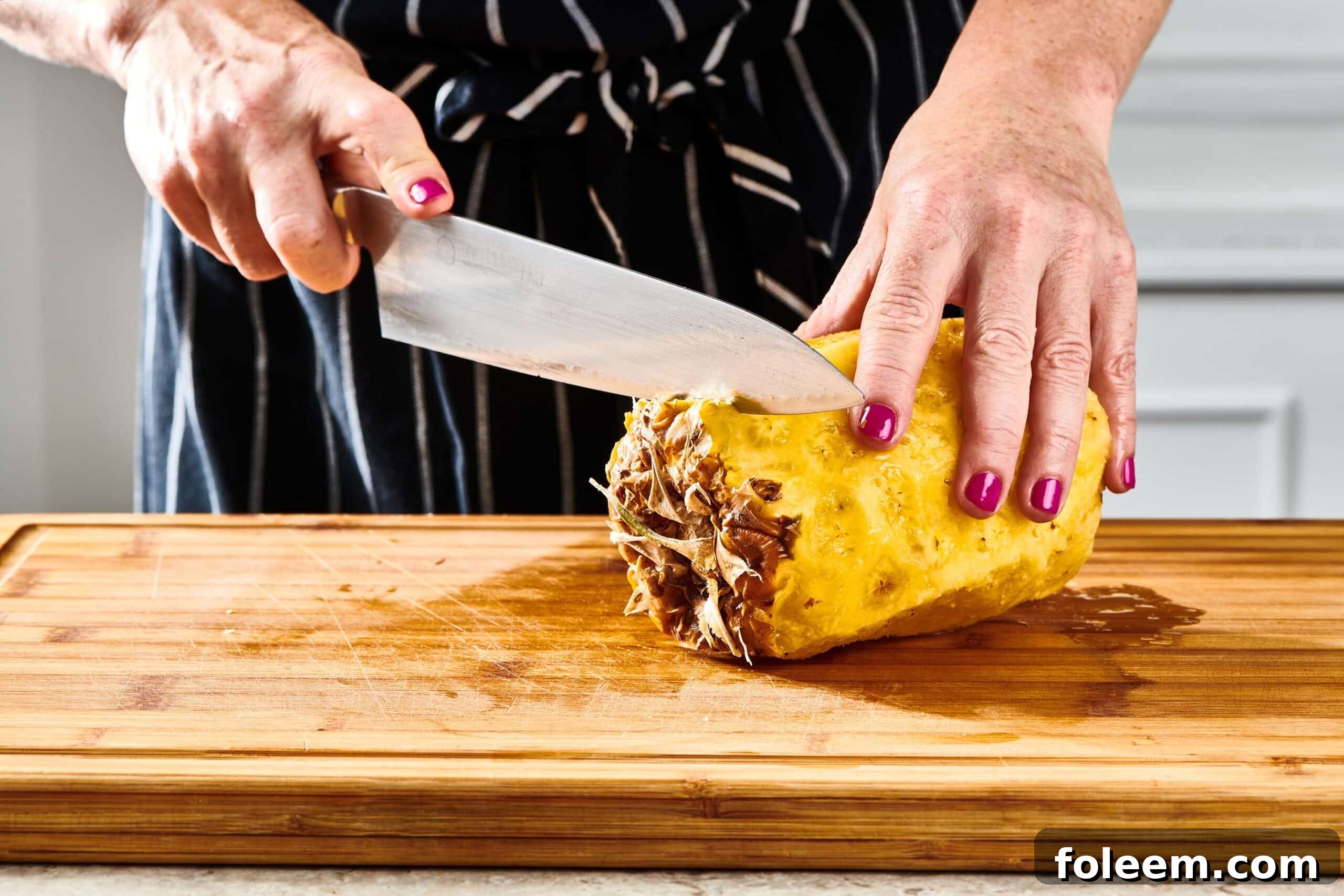 Woman cutting the bottom off of a pineapple.