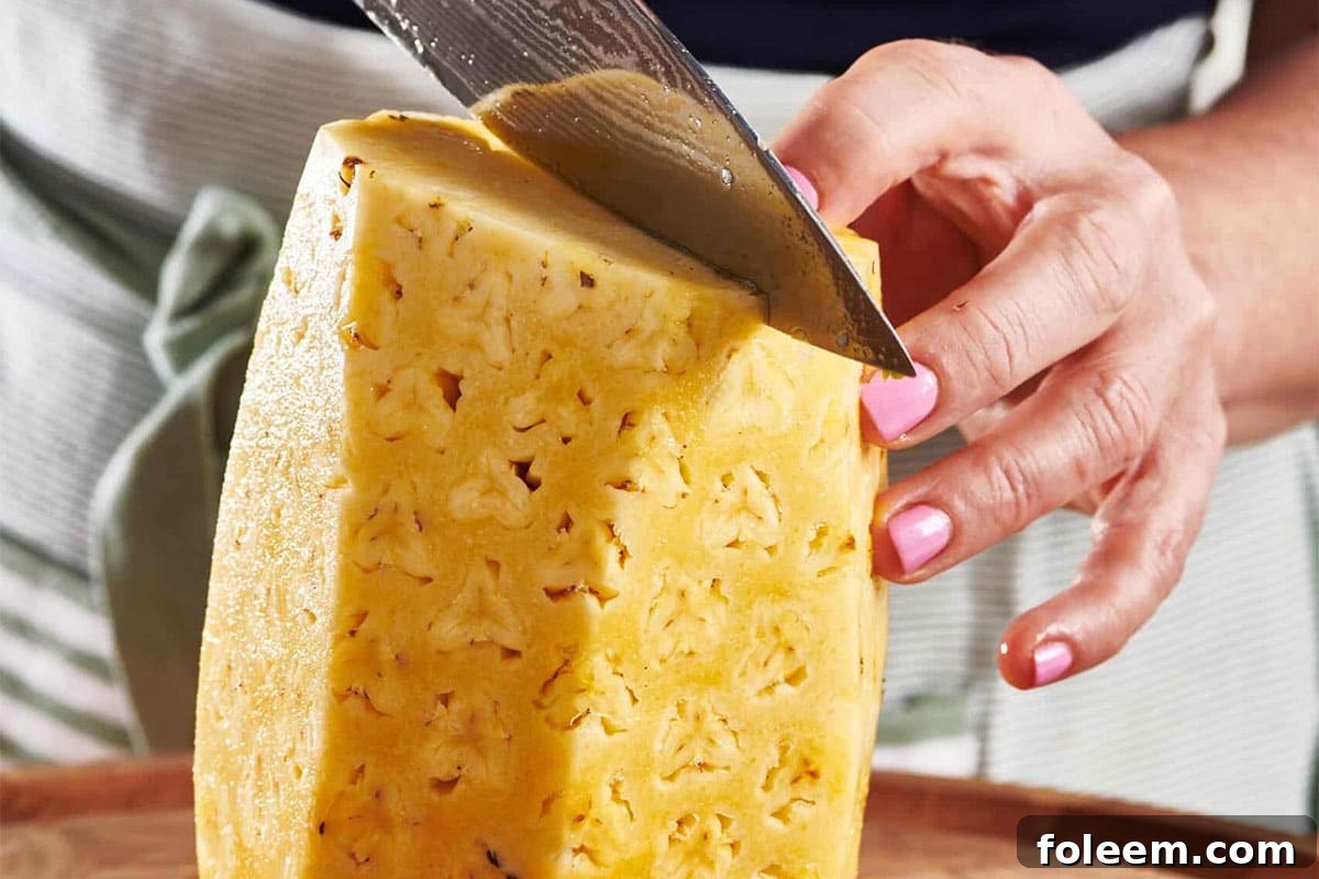 Woman cutting a peeled pineapple in half.
