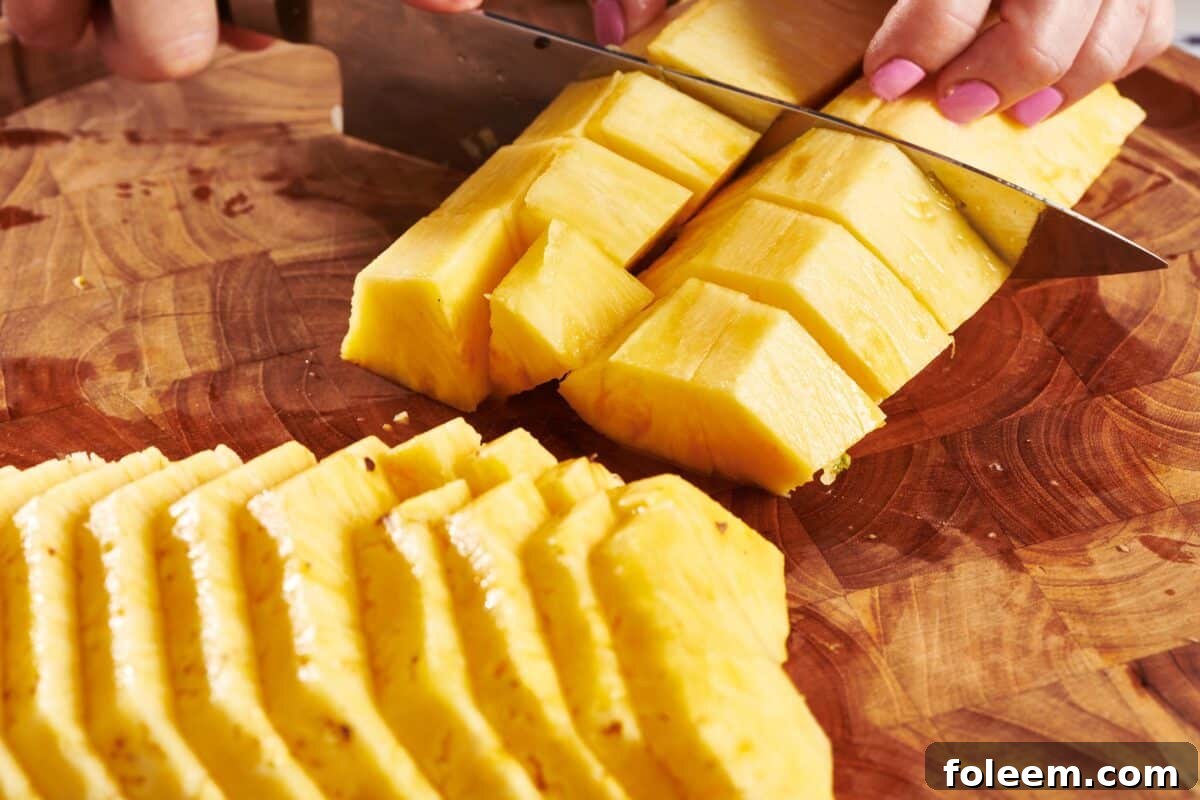 Woman cubing fresh pineapple on cutting board.