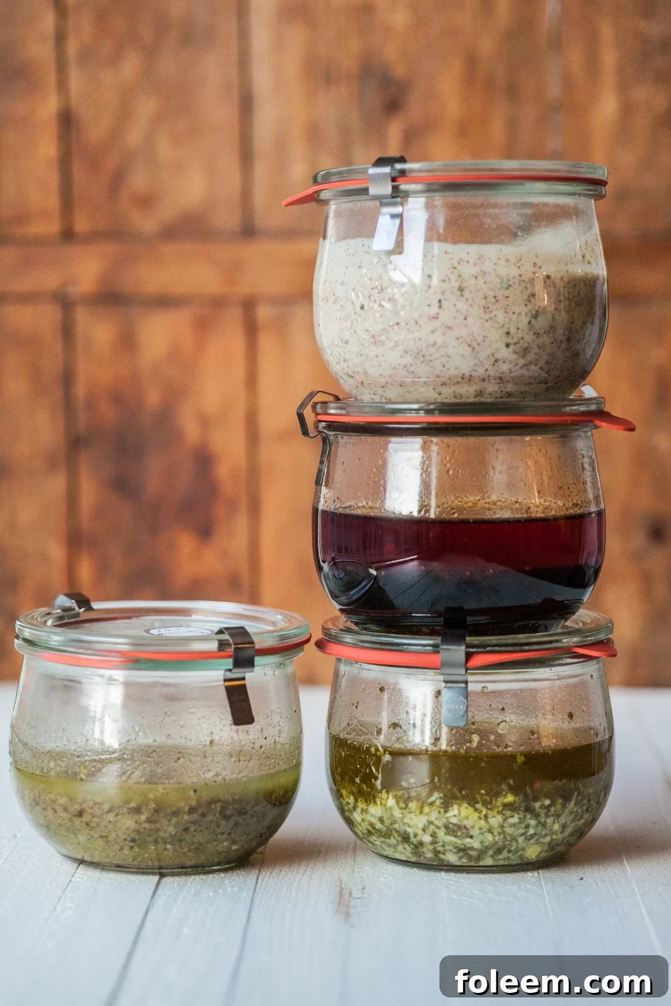 Four marinades in jars stacked on wood counter.