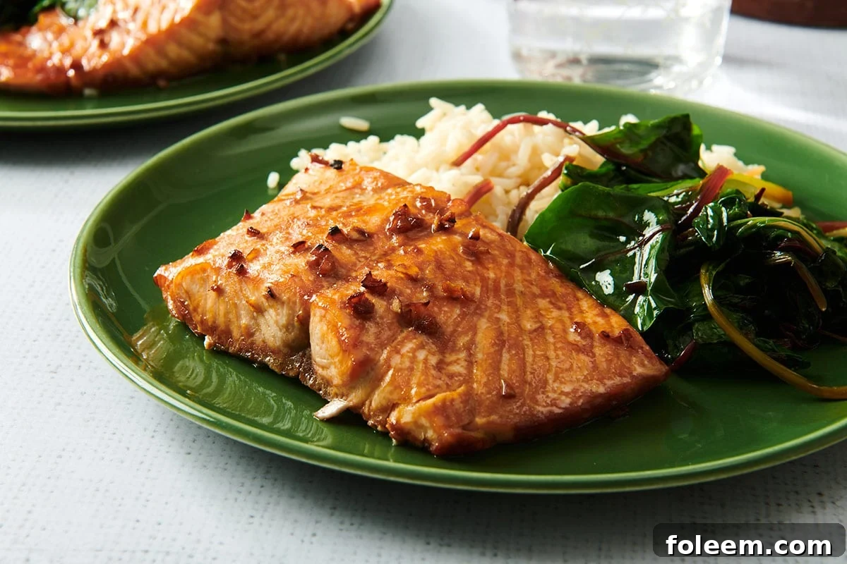 Teriyaki salmon on green plate with a side of sauteed greens and rice.
