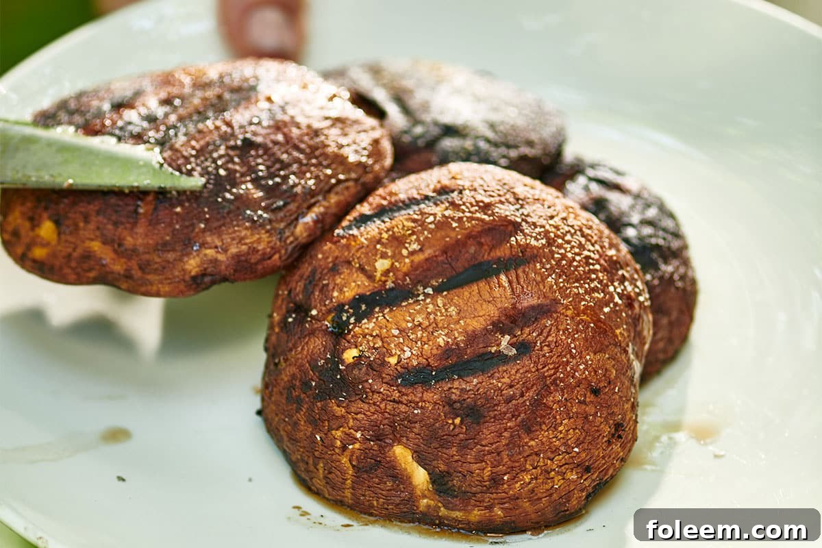 Transferring grilled portobello mushrooms to white plate using barbecue tongs.