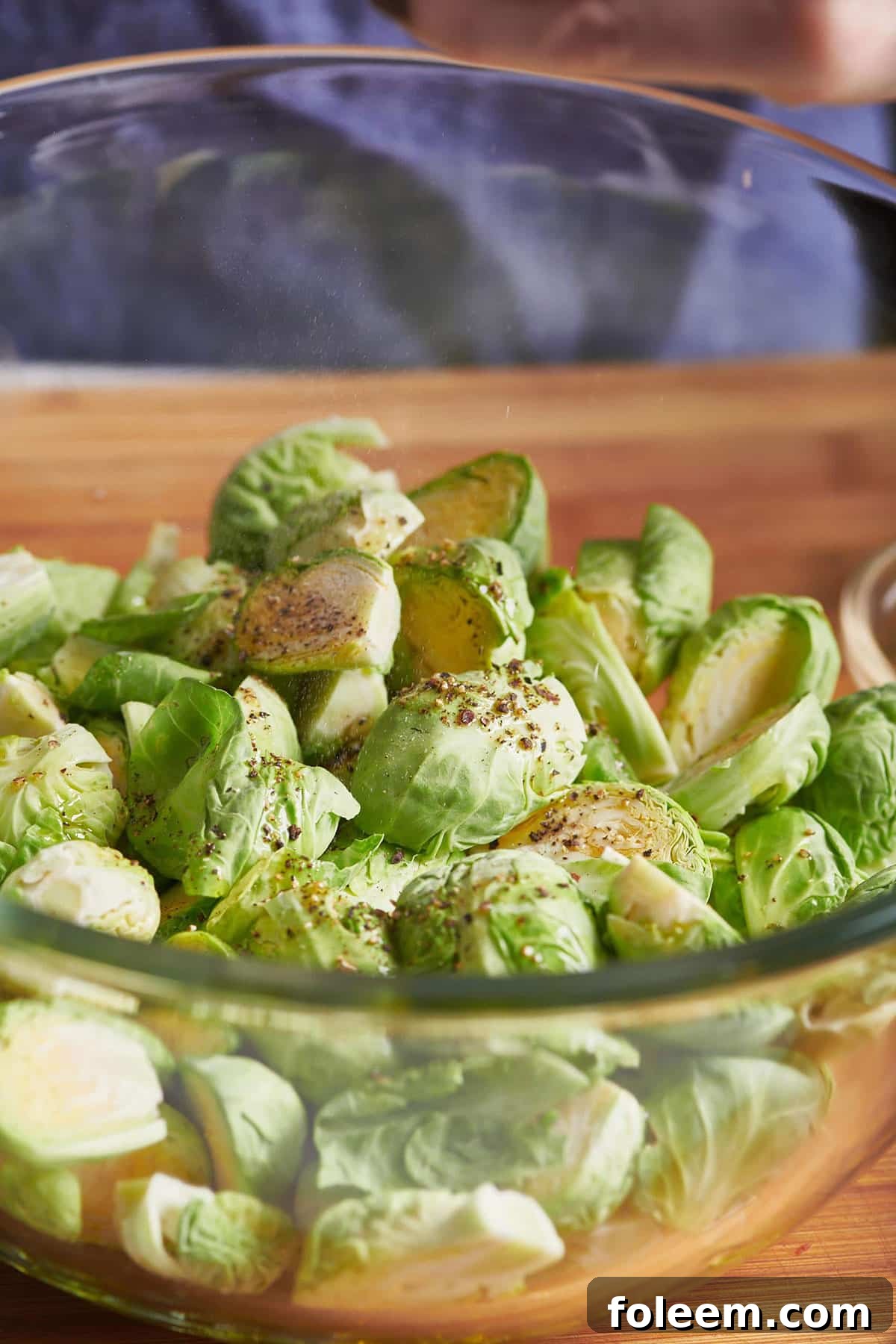 Seasoned, halved brussels sprouts in a glass bowl.