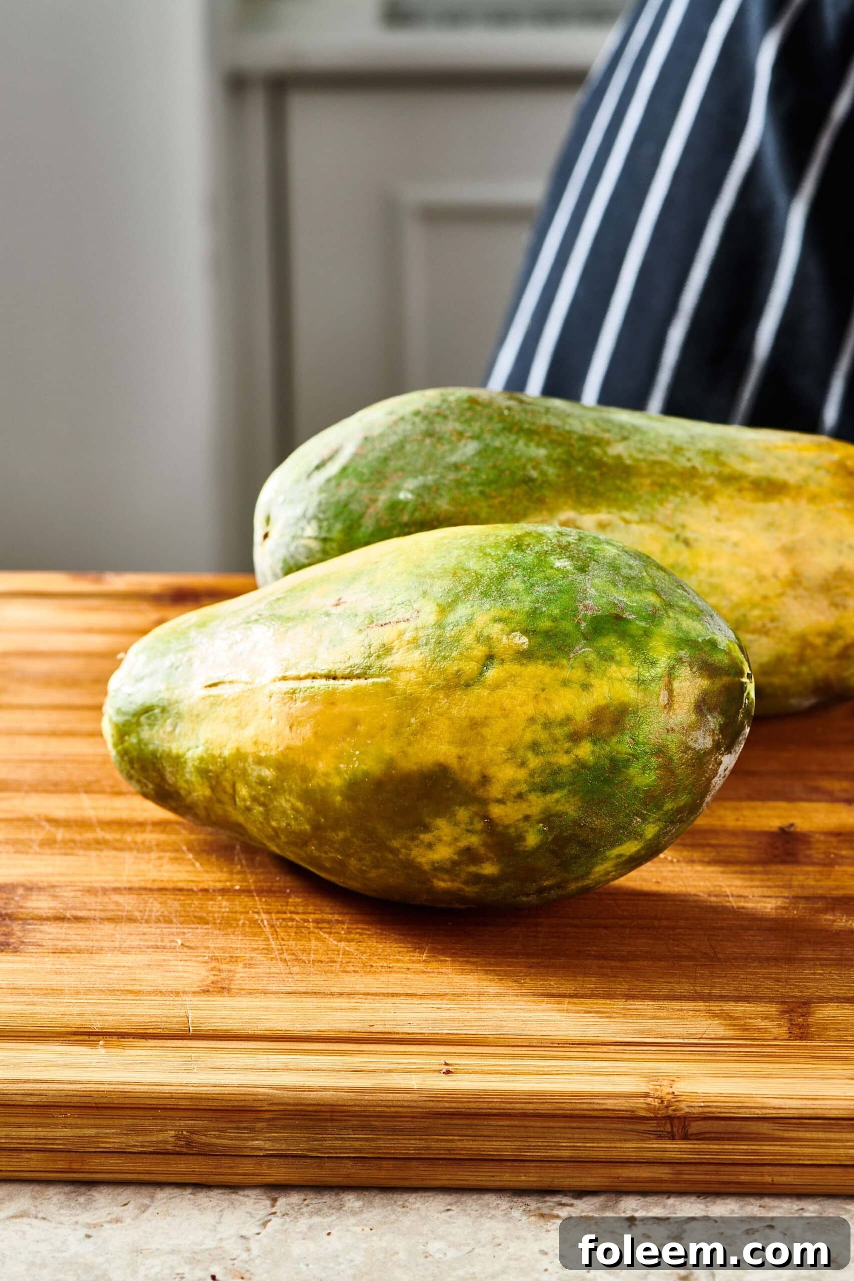 Two Papayas on a wooden cutting board.