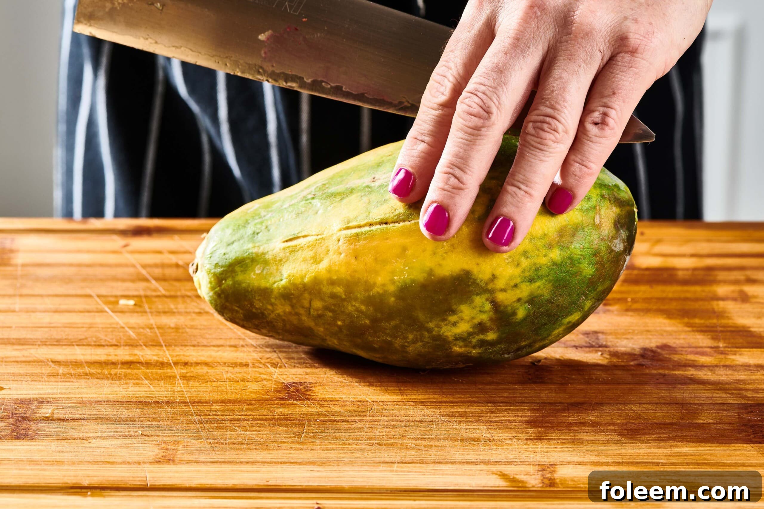 Woman holding a papaya and a large knife.