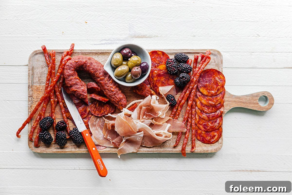 Meat arranged on a board with fruit and a bowl of olives.