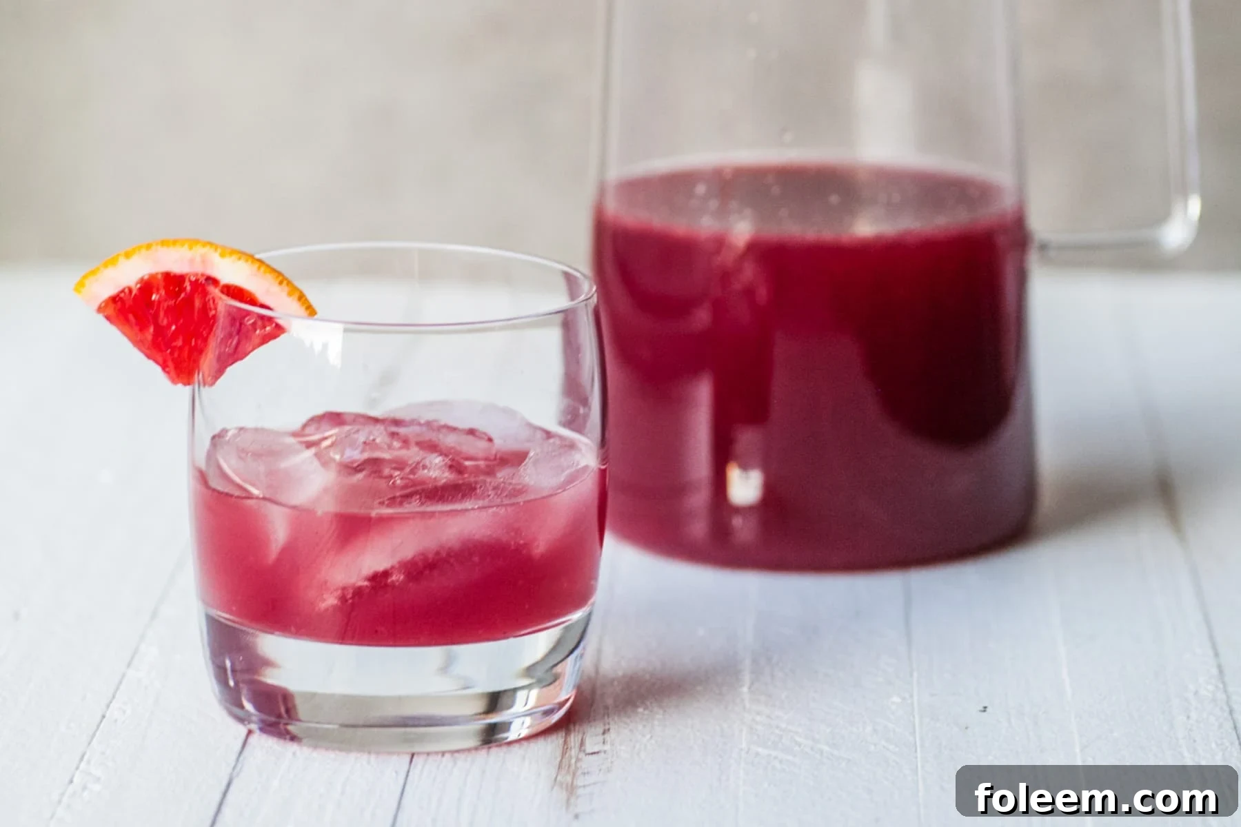 Red cocktail in glass and pitcher on table.