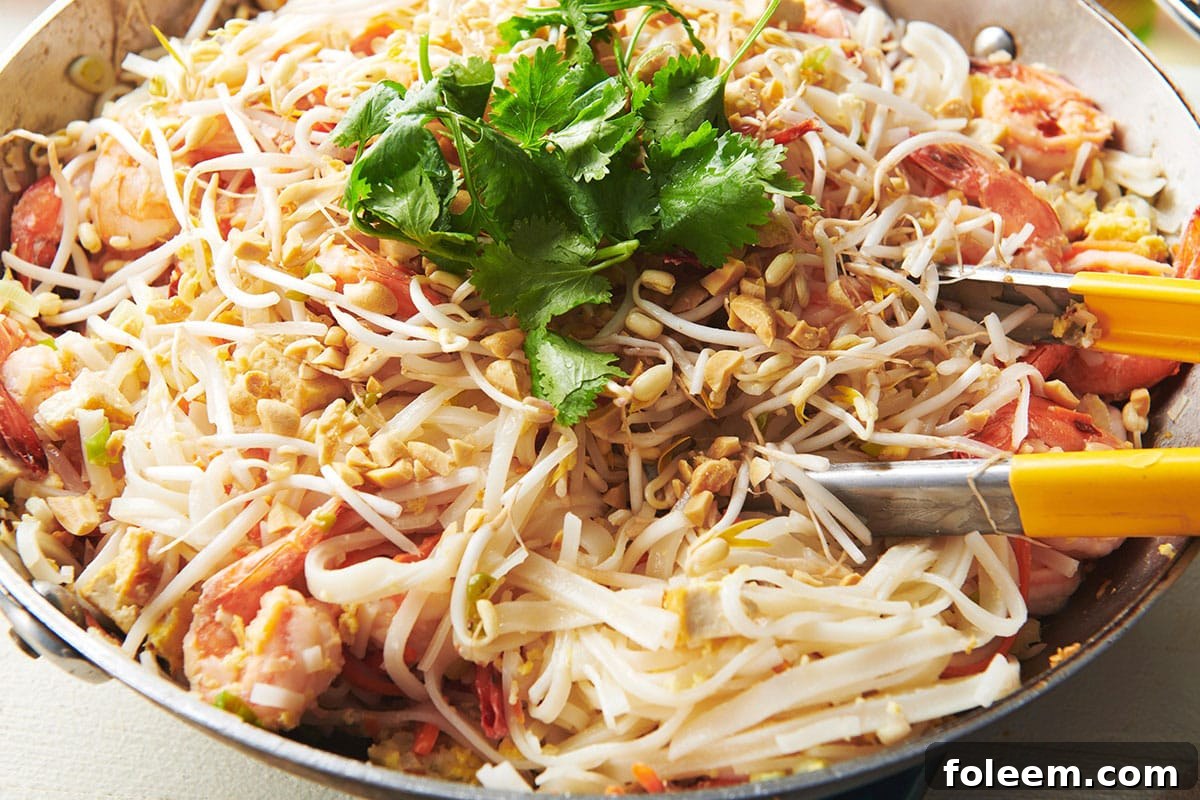 Tongs in a wok of Pad Thai.