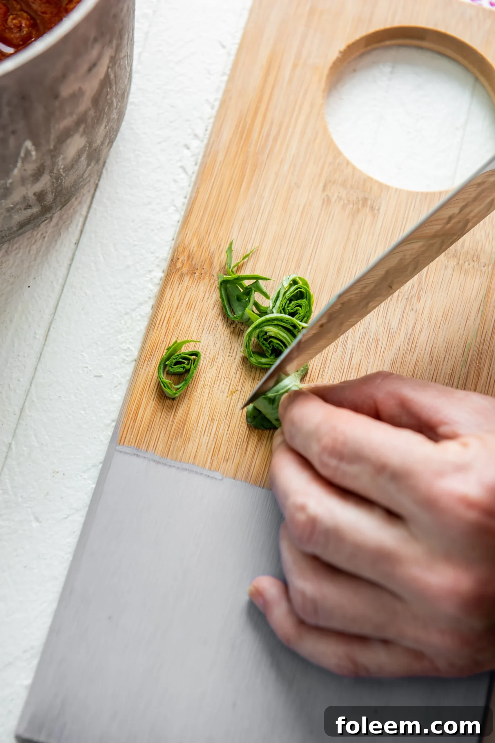 Woman cutting basil into chiffonade strips on a painted cutting board.