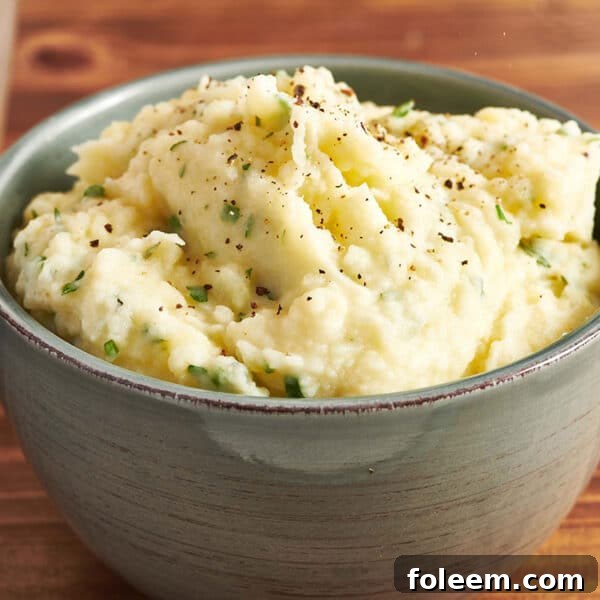 Mashed potatoes with herbs in grey bowl on table.