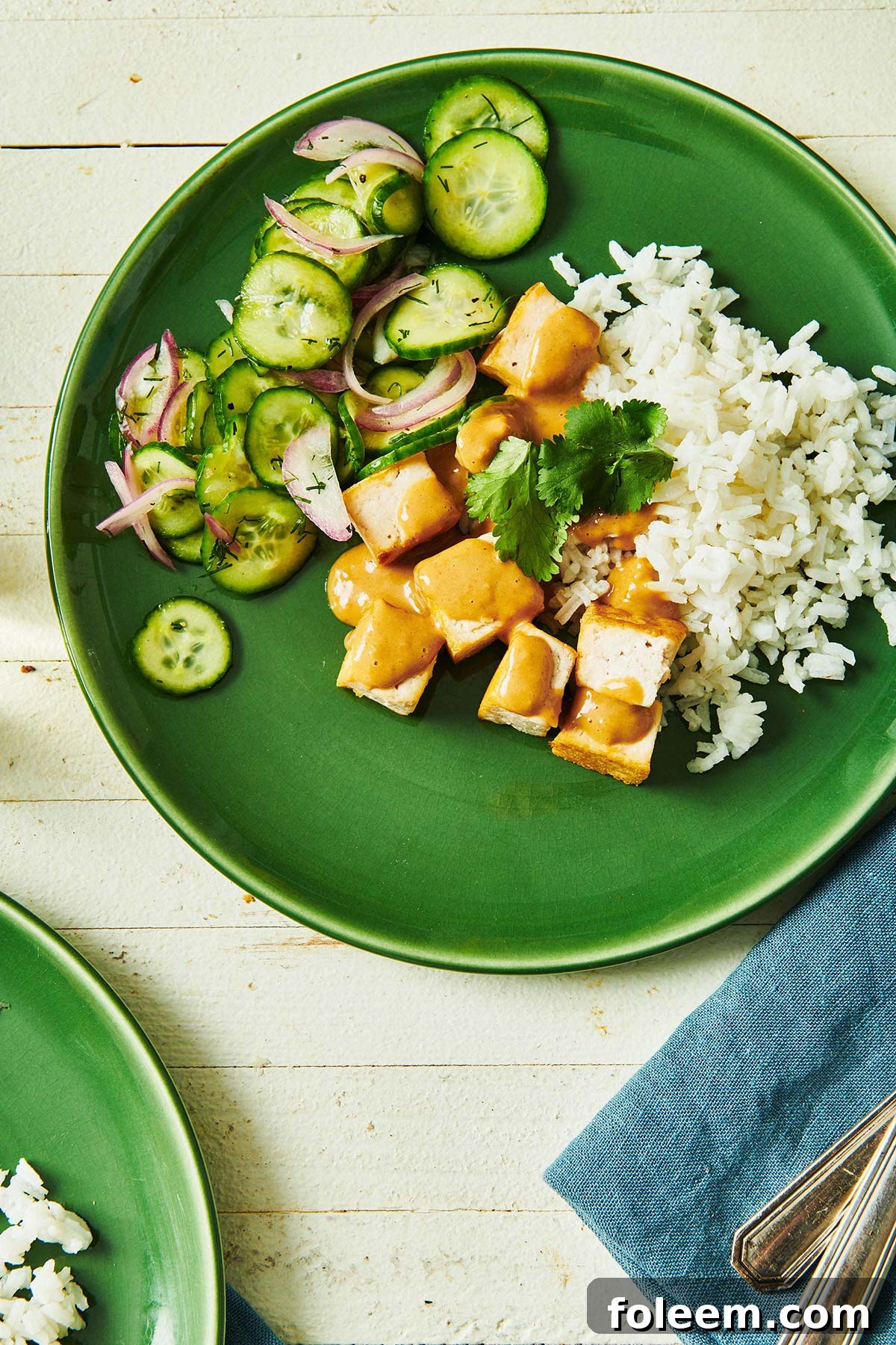 Tofu with Peanut Sauce on a green plate with rice and cucumber salad.