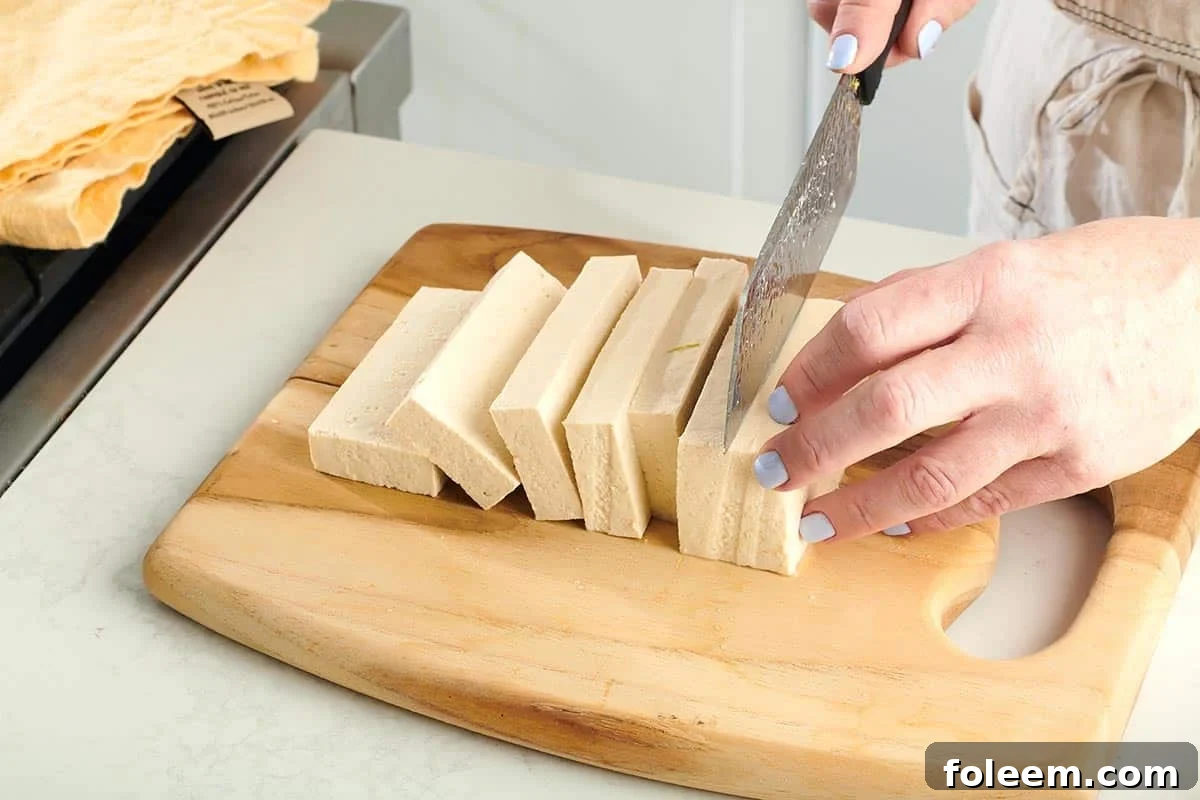 Woman slicing tofu on a wooden cutting board.