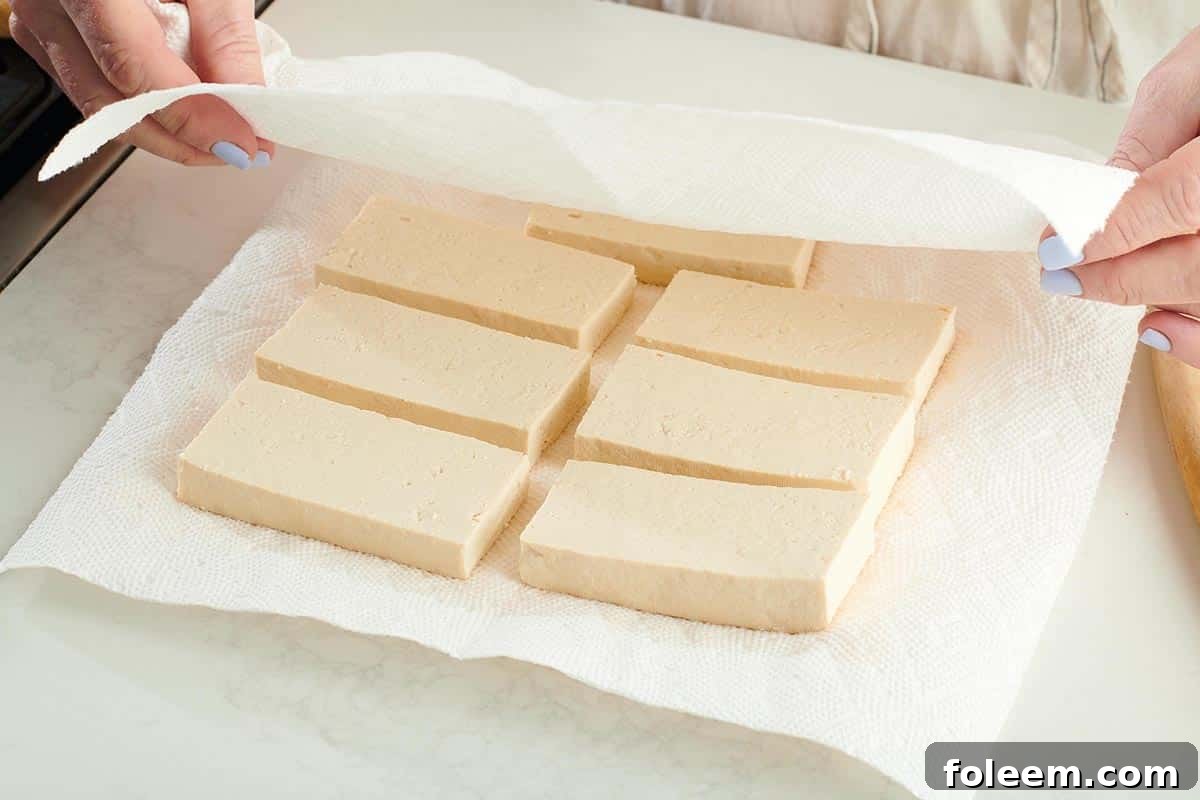 Covering sliced tofu with paper towels to press out moisture.