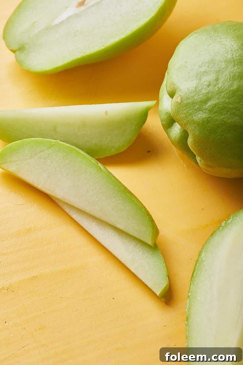 Whole and sliced fresh chayote on wood.