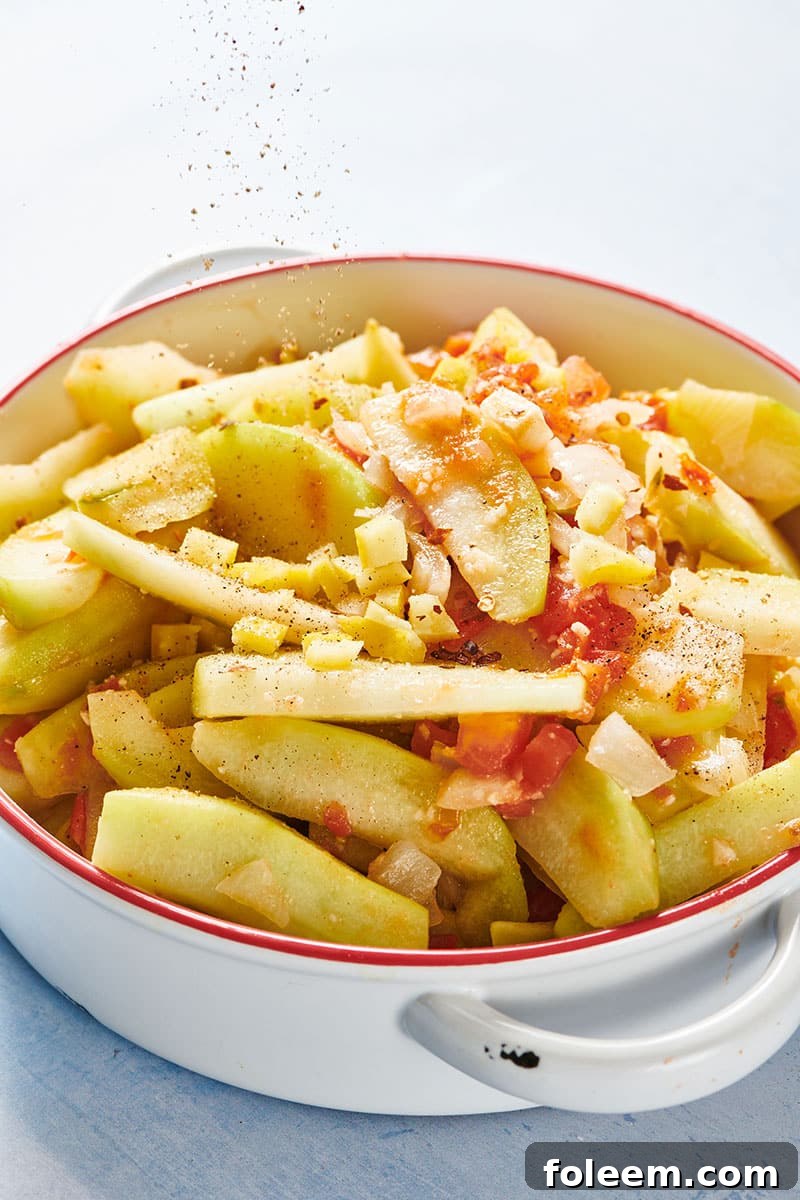 Stewed chayote with onion and tomato in white cooking pot.