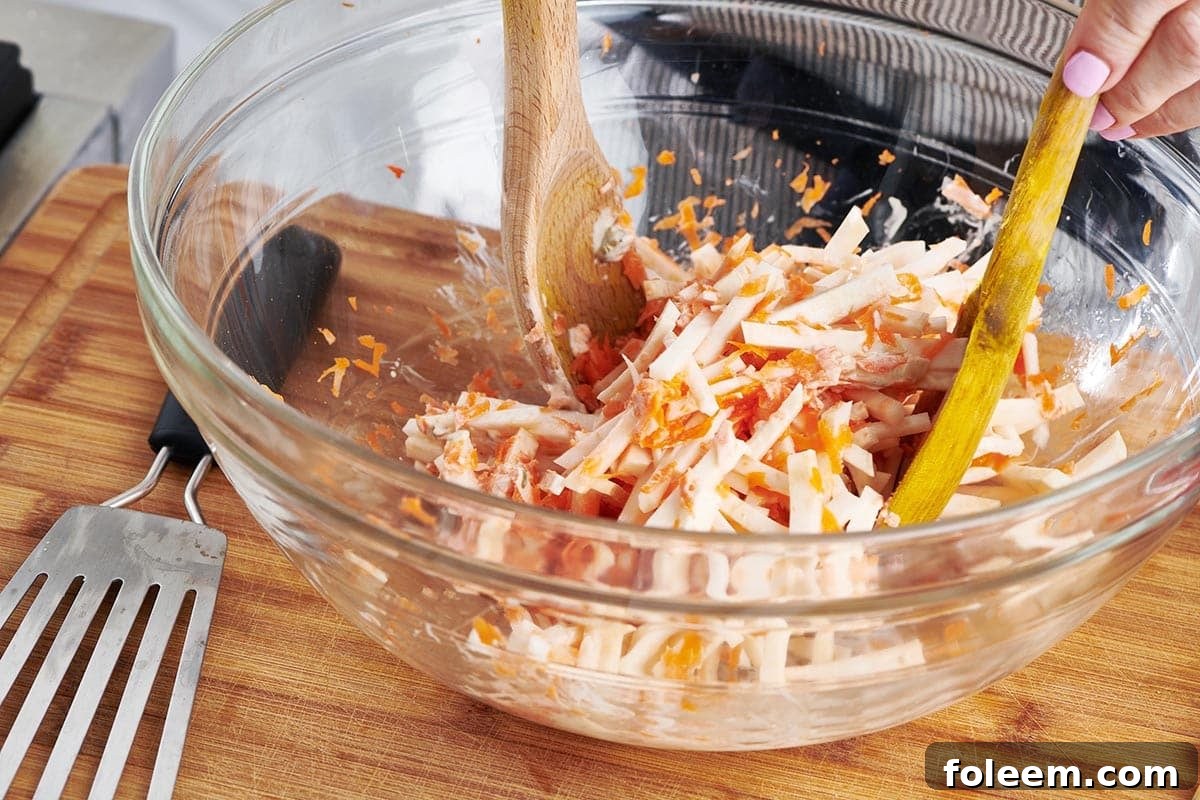 Woman tossing Carrot Celeriac Remoulade in a bowl.