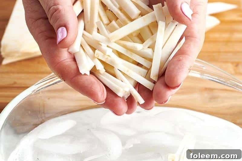 Woman placing sliced celeriac into ice water bowl.