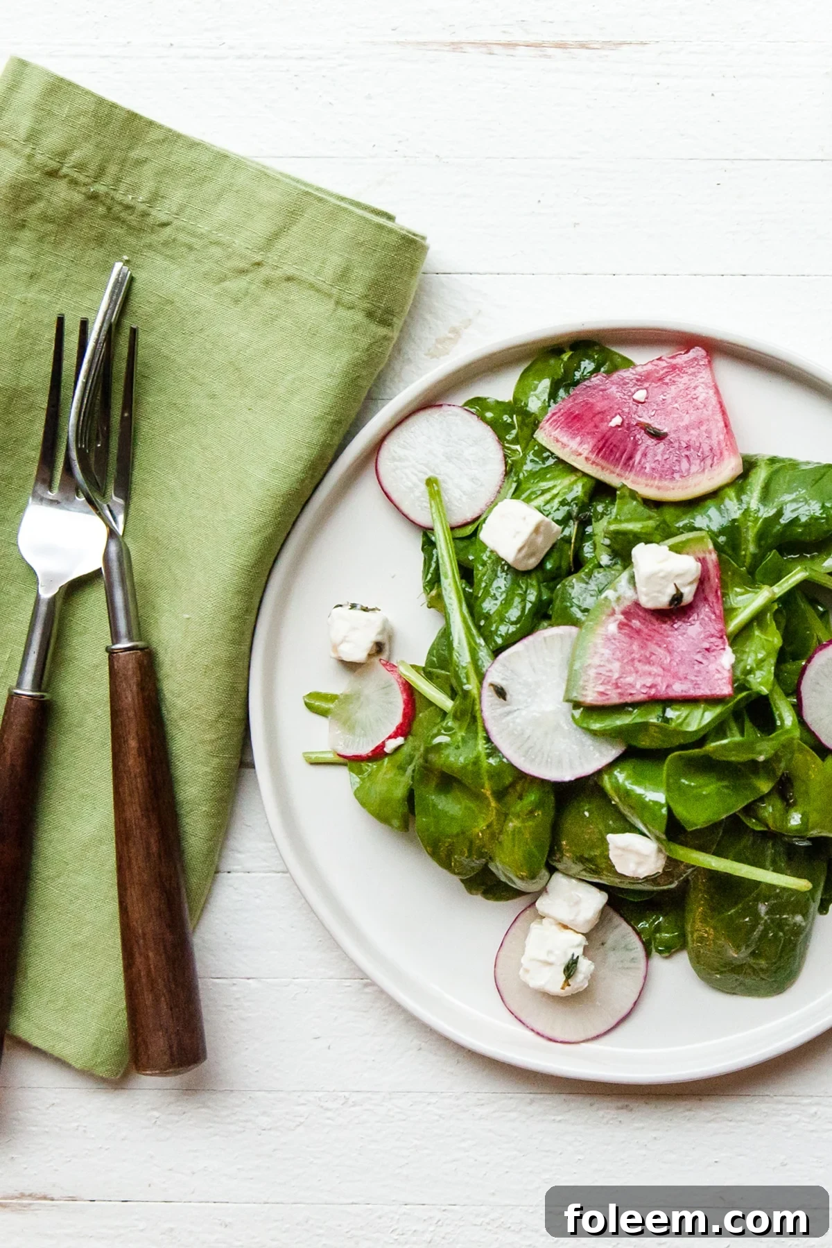 White plate of spinach and radish salad with feta.