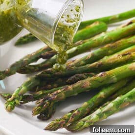 Pouring scallion chimichurri sauce over grilled asparagus on plate.