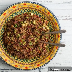 Two spoons in a colorful bowl of Lentil, Red Onion and Avocado Salad.