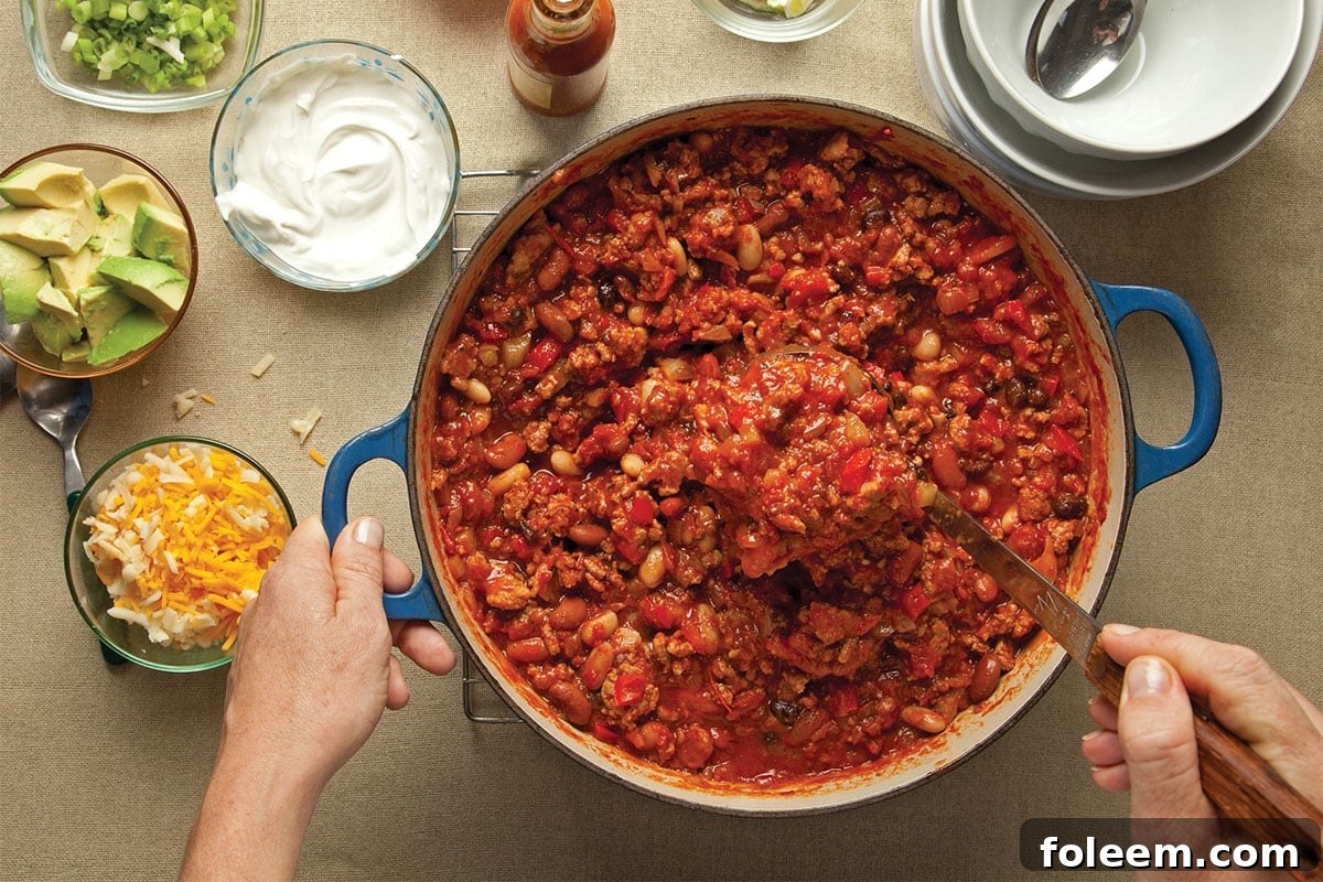 Serving turkey chili from pot next to chili toppings.