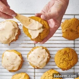 Adding icing to pumpkin cookies with kitchen spatula.