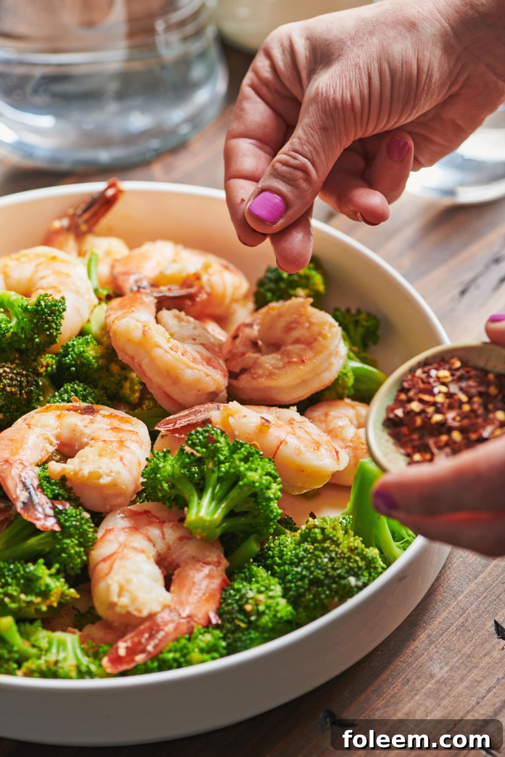 Sprinkling red pepper flakes over Garlicky Shrimp in bowl.