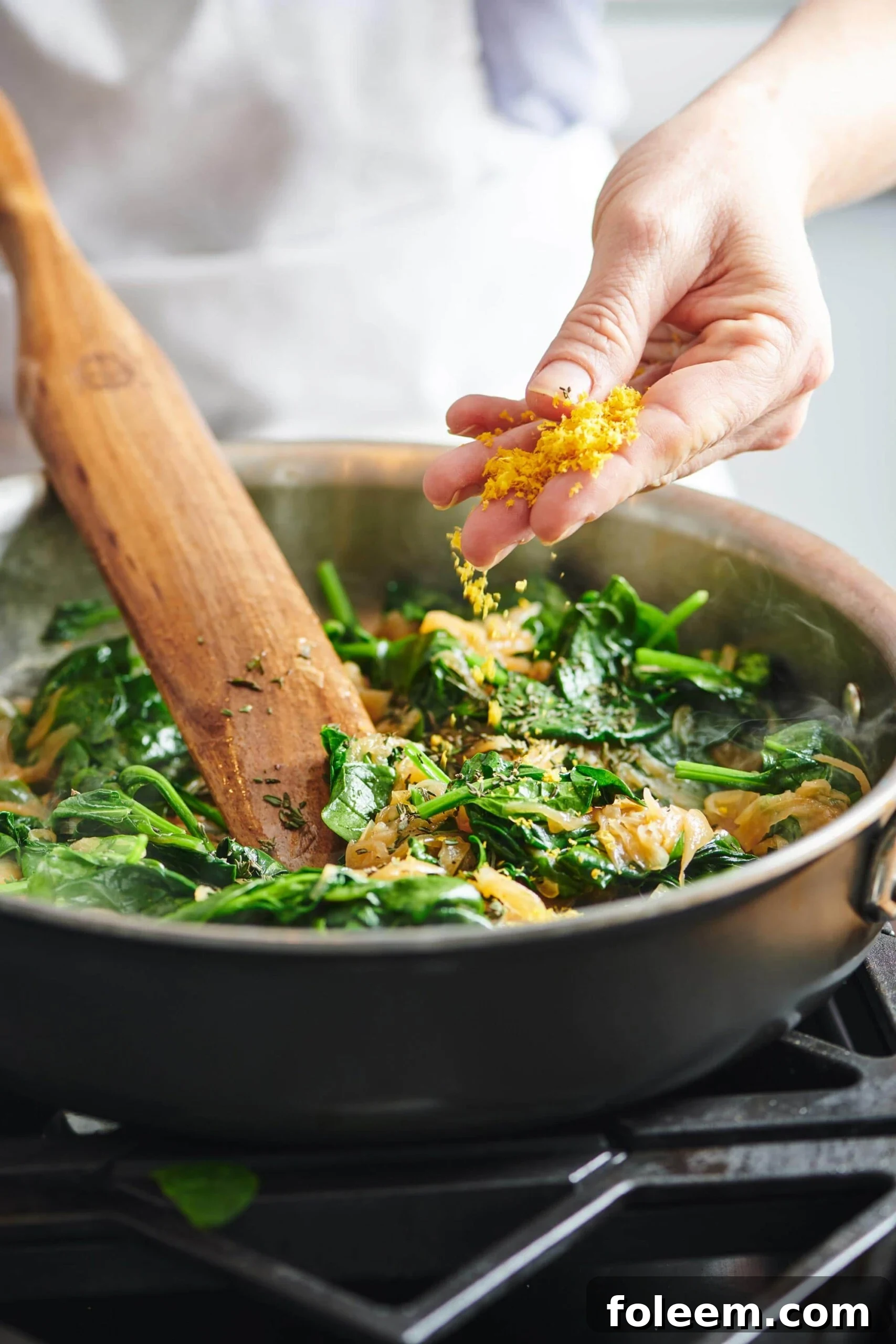 Woman sprinkling lemon zest into a pan of  Spinach.