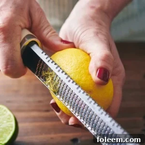 Woman zesting lemon with Microplane over wood cutting board.