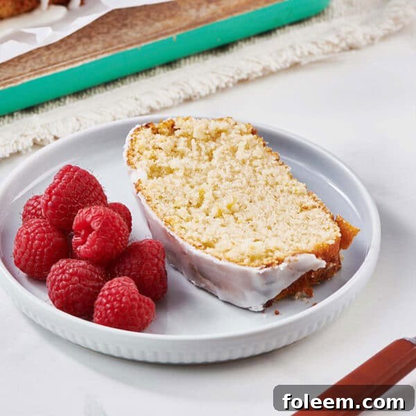 Slice of glazed lemon cake on plate with raspberries.