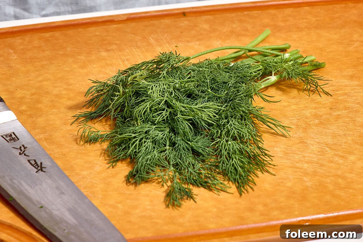 Bunch of fresh dill on wood cutting board next to knife.