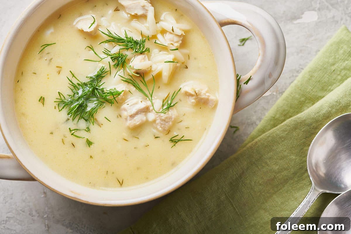 White, handled bowl of Avgolemono Soup with fresh dill.