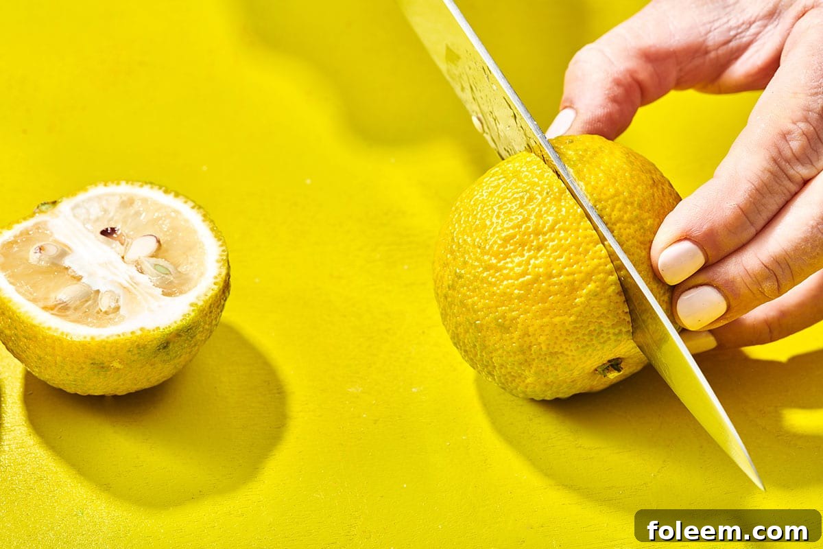 Woman slicing yuzu fruit in half with chef knife on yellow board.