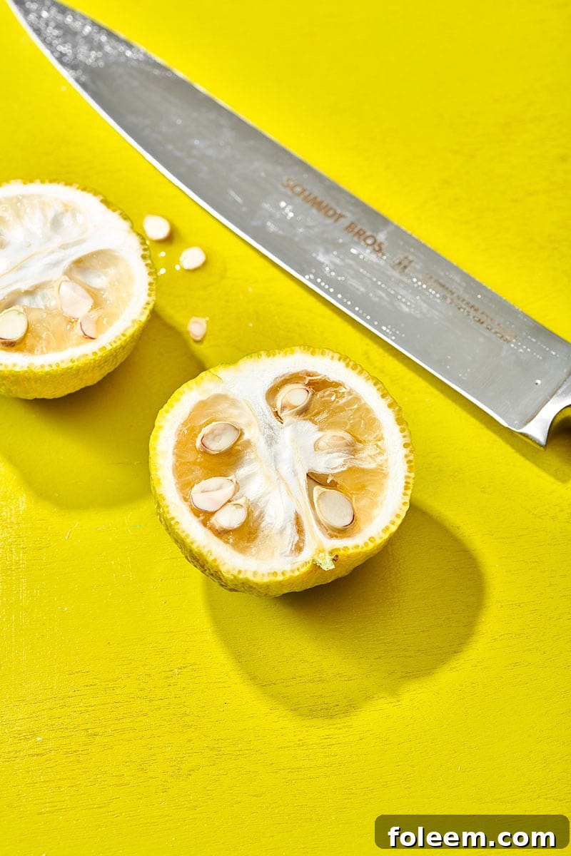 Cut yuzu fruit with chef knife on yellow table.