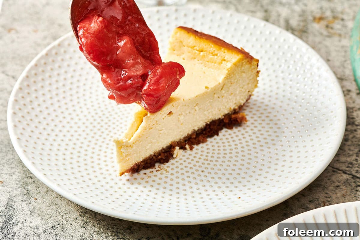 Spreading Strawberry Topping on slice of Cheesecake with spoon.