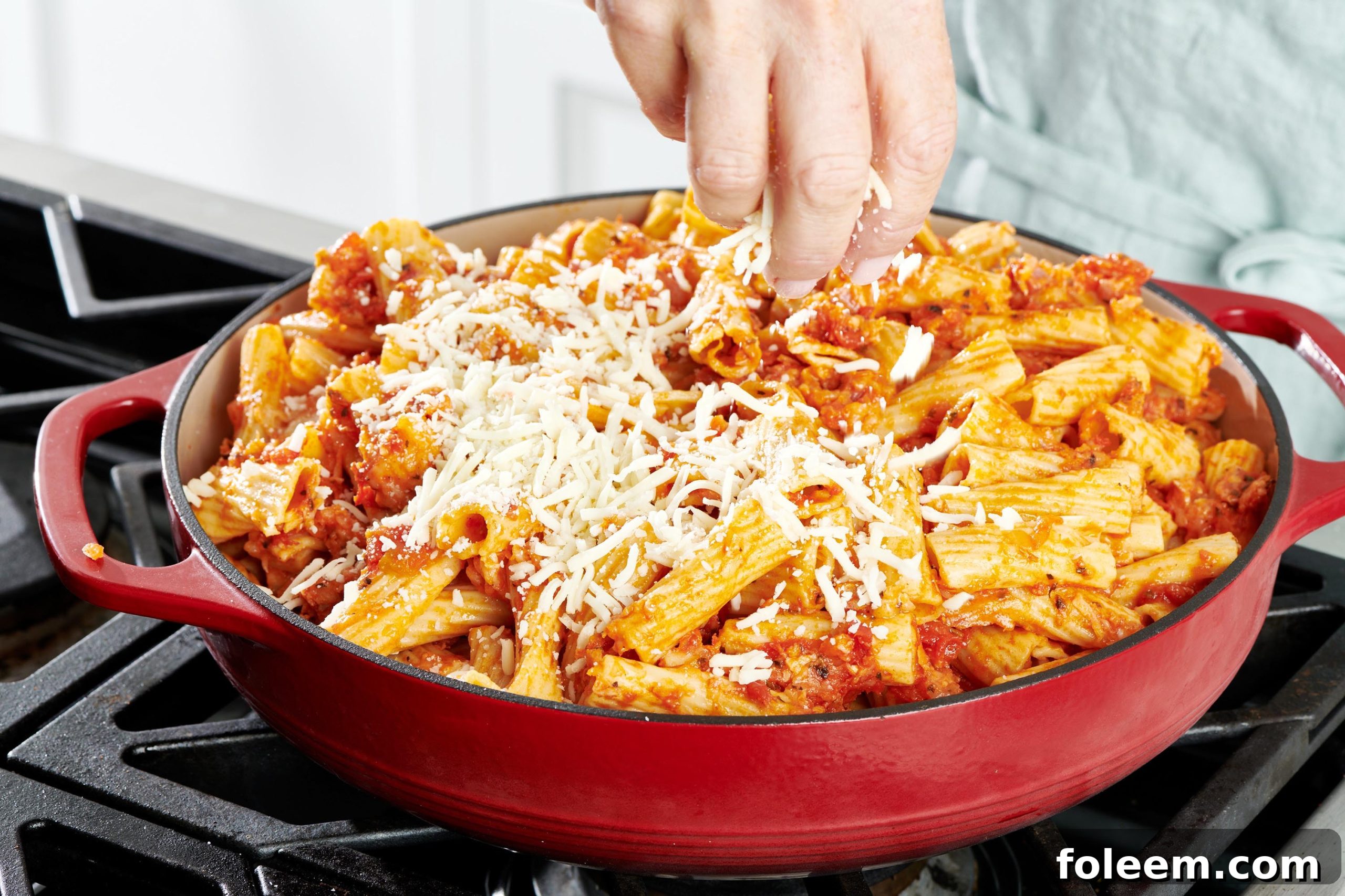Woman sprinkling shredded mozzarella on a dish of ziti.
