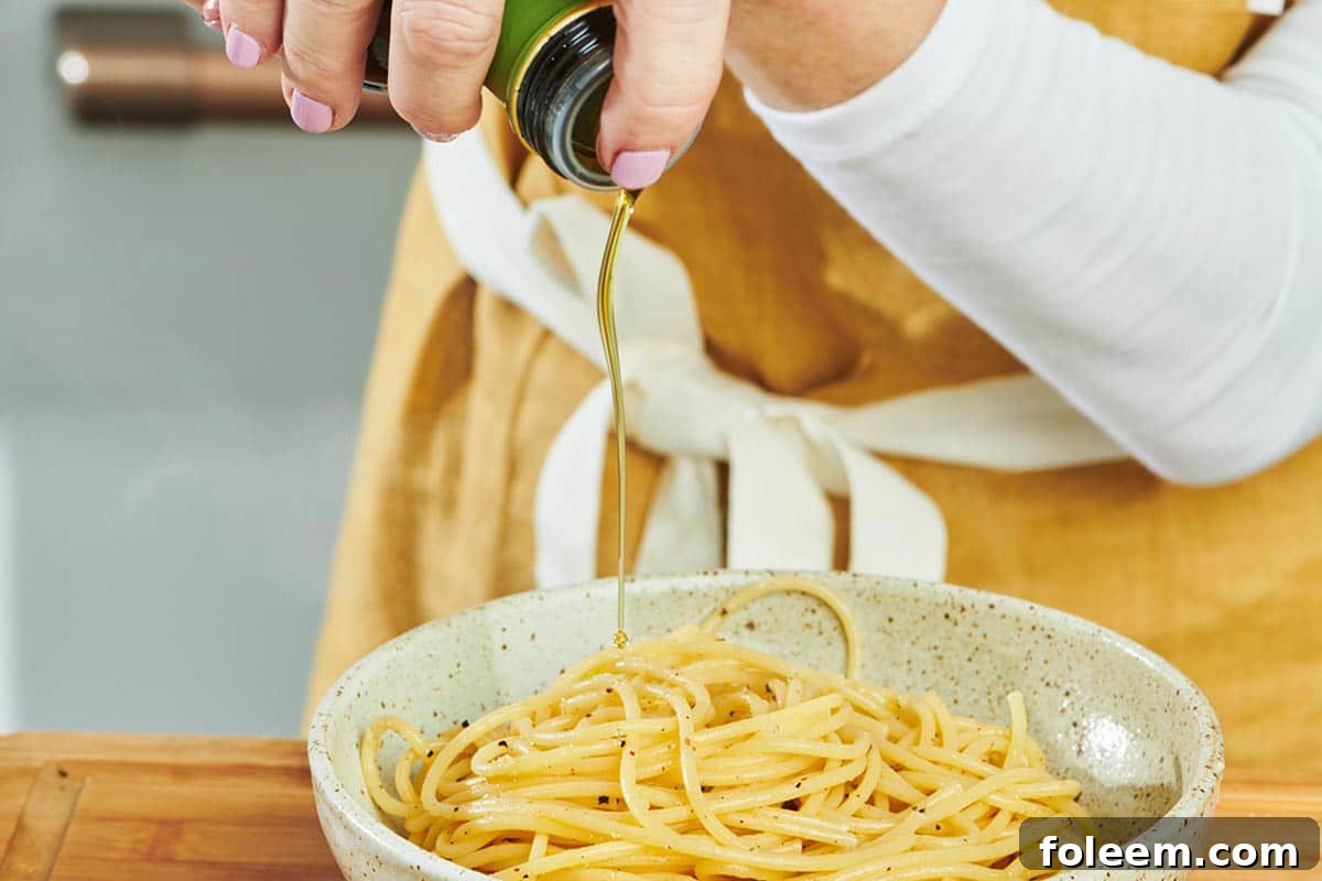 Woman adding oil to bowl of cooked spaghetti.
