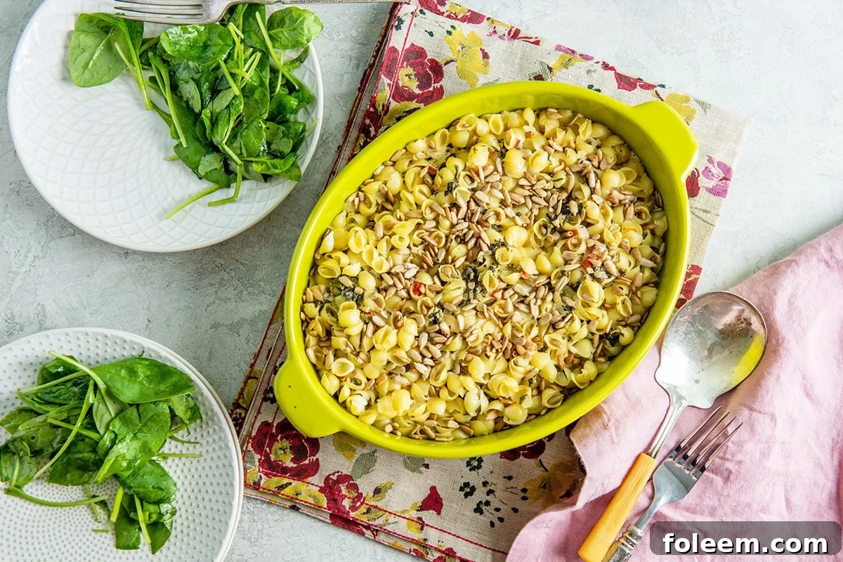 Spinach Goat Cheese Baked Pasta with Sunflower Seeds in yellow dish on table alongside plates with salads.