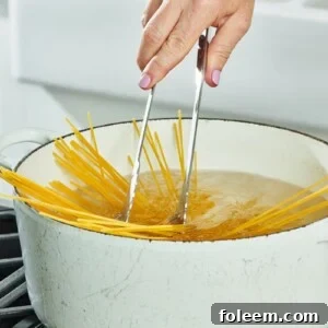 Stirring spaghetti in white pot of boiling water with tongs.